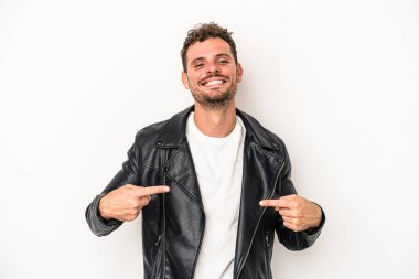 Beyaz arka planda yaşayan beyaz tenli genç bir adam gömlek fotokopi alanını gösteriyor, gururlu ve kendinden emin.