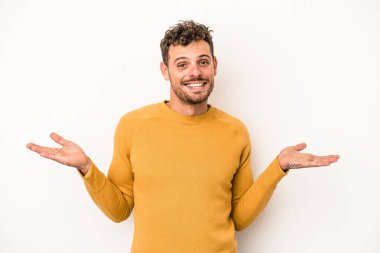 Beyaz arka planda izole genç beyaz adam kollarıyla ölçek yapar, mutlu ve kendinden emin hisseder..