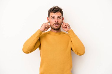 Beyaz arka planda izole edilmiş genç beyaz bir adam parmaklarıyla kulaklarını kapatıyor, gürültülü bir ortam yüzünden stresli ve çaresiz..