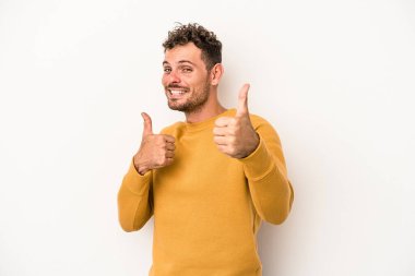 Beyaz arka planda izole edilmiş genç beyaz bir adam iki parmağını da kaldırıyor, gülümsüyor ve kendinden emin..
