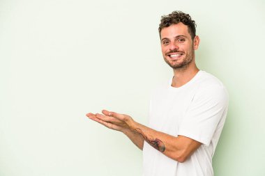 Yeşil arka planda izole edilmiş genç beyaz bir adam palmiyesinde bir kopya alanı tutuyor..