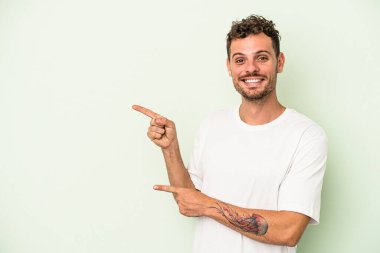 Yeşil arka planda izole edilmiş genç beyaz adam işaret parmaklarıyla işaret ederek heyecanlanıyor..