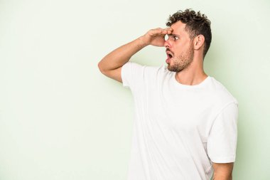 Kafkasyalı genç adam yeşil arka planda izole edilmiş, uzaklara bakıyor ve elini alnına koyuyor..