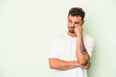 Yeşil arka planda izole edilmiş, üzgün ve dalgın hisseden, fotokopi alanına bakan genç beyaz adam..