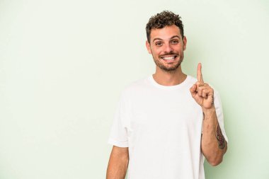 Yeşil arka planda izole edilmiş genç beyaz bir adam bir numarayı parmağıyla gösteriyor..