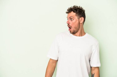 Genç beyaz adam yeşil arka planda izole edilmiş. Gördüğü bir şey yüzünden şoka uğruyor..