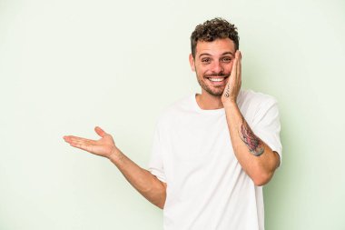 Yeşil arka planda izole edilmiş genç beyaz bir adam bir avuç içinde fotokopi alanı tutuyor, el üstünde tutuyor. Şaşırmış ve mutlu..