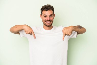 Genç beyaz adam yeşil arka planda izole edildi. Parmakları aşağıda, olumlu bir his var..