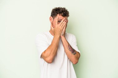Genç beyaz adam yeşil arka planda izole edilmiş. Korkmuş ve gergin parmaklarıyla göz kırp..