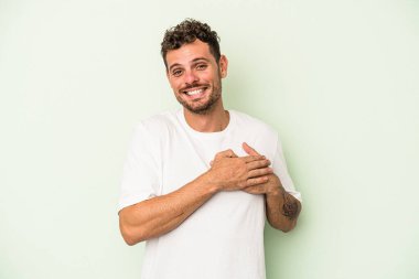 Yeşil arka planda izole edilmiş beyaz bir genç, dost canlısı bir ifadeye sahip, avuçlarını göğsüne bastırıyor. Aşk konsepti.