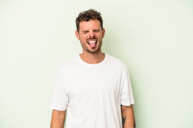 Genç beyaz adam yeşil arka planda izole edilmiş komik ve dost canlısı bir dil uzatıyor..