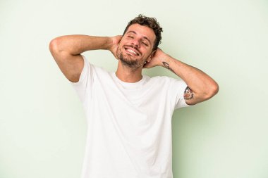 Kafkasyalı genç adam yeşil arka planda izole edilmiş. Kendine güveniyor, elleri başının arkasında..