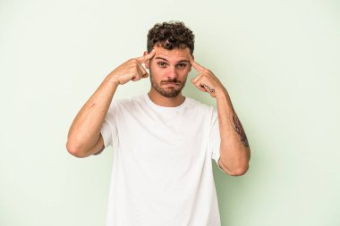 Kafkasyalı genç adam yeşil arka planda izole edilmiş bir göreve odaklanmış, parmaklarını işaret ediyor..