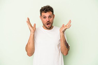 Yeşil arka planda izole genç beyaz adam şaşırdı ve şok oldu..