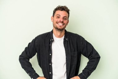 Kafkasyalı genç adam yeşil arka planda izole edilmiş. Kendine güveniyor. Kalçaları tutuyor..