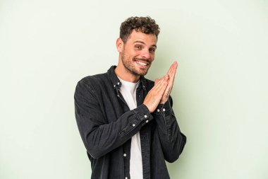 Genç beyaz adam yeşil arka planda izole edilmiş enerjik ve rahat hissediyor, ellerini ovuşturuyor kendinden emin..