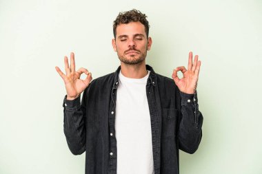 Yeşil arka planda izole edilmiş genç beyaz adam yoğun bir günün ardından rahatlıyor. Yoga yapıyor..