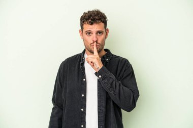 Yeşil arka planda izole edilmiş genç beyaz bir adam ya sır saklıyor ya da sessizlik istiyor..
