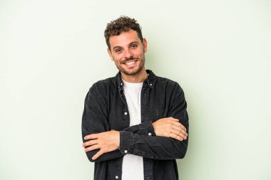 Yeşil arka planda kendini güvende hisseden, kararlı kollarını kavuşturan genç beyaz bir adam..