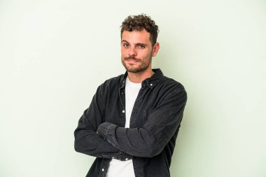 Genç beyaz adam yeşil arka planda izole edilmiş şüpheli, belirsiz, seni inceliyor..