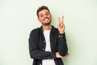 Yeşil arka planda izole edilmiş genç beyaz adam iki numarayı parmaklarıyla gösteriyor..