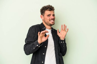 Yeşil arka planda izole edilmiş genç beyaz adam tiksinti belirtisi gösteren birini reddediyor..