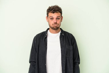 Yeşil arka planda izole genç beyaz adam yanakları patlatır, yorgun bir ifadeye sahiptir. Yüz ifadesi kavramı.