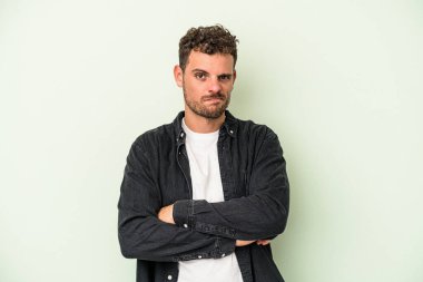 Kafkasyalı genç adam yeşil arka planda izole edilmiş. Mutsuz, iğneleyici bir ifadeyle kameraya bakıyor..