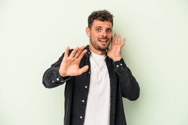 Yeşil arka planda izole genç beyaz adam yakın bir tehlike nedeniyle şoka uğruyor.