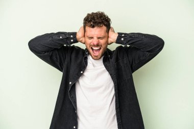 Kafkasyalı genç adam yeşil arka planda izole edilmiş kulakları kulaklarıyla kapatıyor çok fazla ses duymamaya çalışıyor..