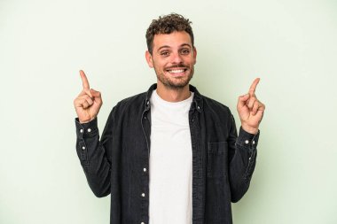 Yeşil arka planda izole genç beyaz adam işaret iki ön parmakları boş bir boşluk gösteren.