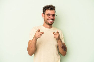 Yeşil arka planda izole edilmiş genç beyaz adam parmaklarıyla ön tarafı işaret ediyor..