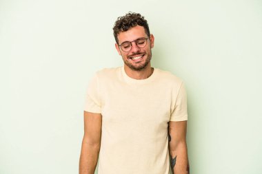 Yeşil arka planda izole edilmiş genç beyaz adam gülüyor ve gözlerini kapıyor, rahatlamış ve mutlu hissediyor..