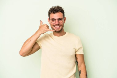 Yeşil arka planda izole edilmiş genç beyaz adam parmaklarıyla bir cep telefonu hareketi gösteriyor..