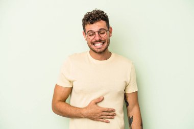 Yeşil arka planda izole edilmiş genç beyaz adam karnına dokunuyor, nazikçe gülümsüyor, yemek yiyor ve tatmin oluyor..