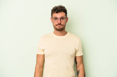 Kafkasyalı genç adam yeşil arka planda izole edilmiş üzgün, ciddi yüzlü, mutsuz ve hoşnutsuz..