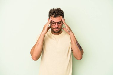 Genç beyaz adam yeşil arka planda izole edilmiş tapınaklara dokunuyor ve baş ağrısı çekiyor..