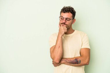 Yeşil arka planda izole edilmiş genç beyaz adam şüpheli ve şüpheci bir ifadeyle yana bakıyor..