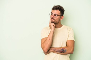 Yeşil arka planda izole edilmiş genç beyaz adam şüpheli ve şüpheci bir ifadeyle yana bakıyor..
