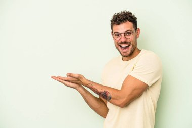 Yeşil arka planda izole edilmiş genç beyaz bir adam palmiyesinde bir kopya alanı tutuyor..