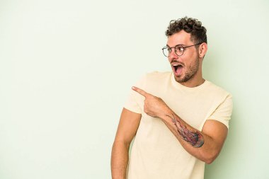 Kafkasyalı genç adam yeşil arka plan noktalarında izole edilmiş başparmak uzakta, gülüyor ve kaygısız.