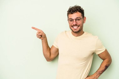 Yeşil arka planda izole edilmiş genç beyaz adam işaret parmağıyla işaret ederek gülümsüyor..