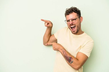 Yeşil arka planda izole edilmiş genç beyaz adam işaret parmaklarıyla işaret ederek heyecanlanıyor..