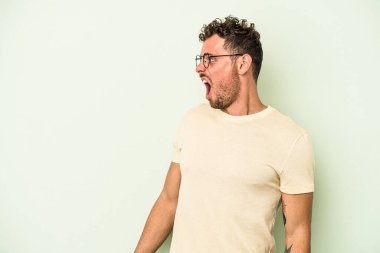 Kafkas 'lı genç adam yeşil arka planda izole edilmiş çok kızgın, öfkeli, hayal kırıklığına uğramış bağırıyor..