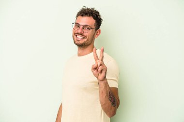 Yeşil arka planda izole edilmiş genç beyaz adam zafer işareti gösteriyor ve gülümsüyor..