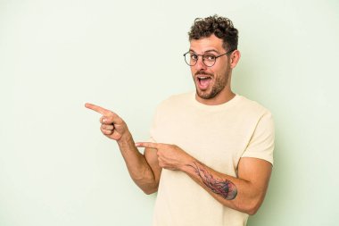 Yeşil arka planda izole edilmiş genç beyaz adam işaret parmağıyla fotokopi alanını işaret ederek heyecan ve arzusunu ifade ediyor..