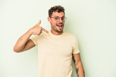 Yeşil arka planda izole edilmiş genç beyaz bir adam tişört fotokopi alanını gösteriyor, gururlu ve kendinden emin.