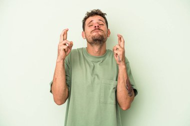 Yeşil arka planda izole genç beyaz adam şans dilemek için şans diliyor.