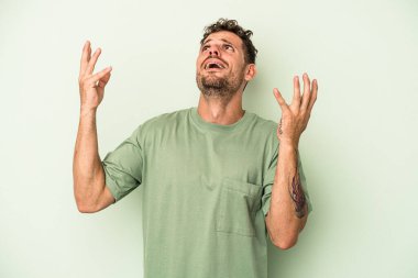 Kafkasyalı genç adam yeşil arka planda izole edilmiş gökyüzüne bağırıyor, yukarı bakıyor, hayal kırıklığına uğramış..