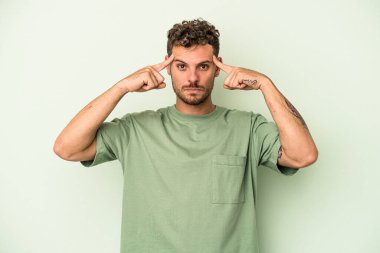 Kafkasyalı genç adam yeşil arka planda izole edilmiş bir göreve odaklanmış, parmaklarını işaret ediyor..